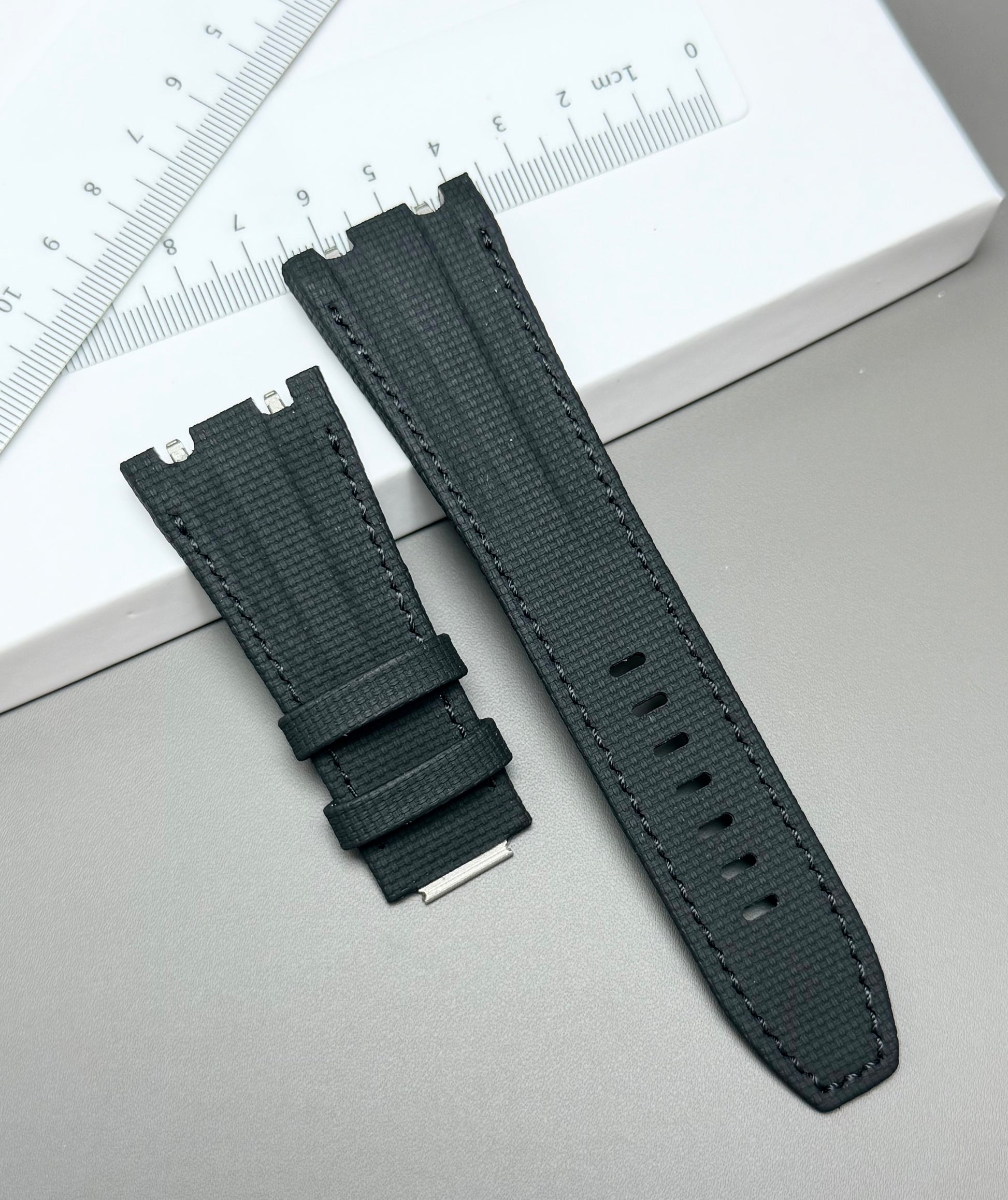 Black watch strap on a light gray surface with a ruler in the background